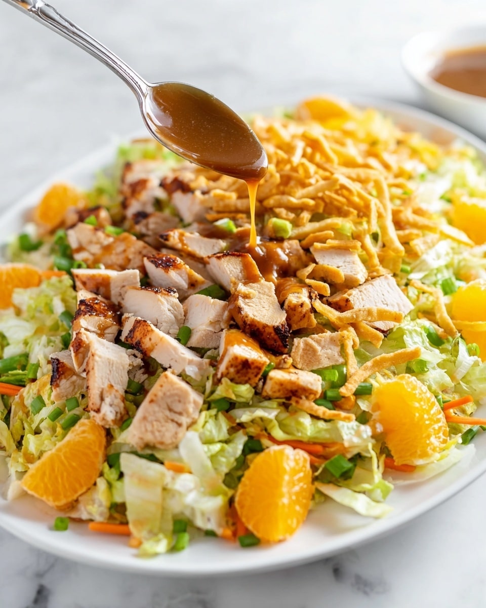 A white plate holds a colorful salad with several visible layers. The base layer is light green chopped lettuce with some orange carrot strips mixed in. On top of that are bright orange mandarin slices scattered around. Cubes of light brown grilled chicken with a slight char are placed evenly across the salad. Thin, light golden crispy strips are layered on, along with chopped green onions adding a fresh touch. A spoon is held over the salad, pouring a smooth, thick brown dressing onto the chicken and mandarin pieces. The plate sits on a white marbled surface. photo taken with an iphone --ar 4:5 --v 7