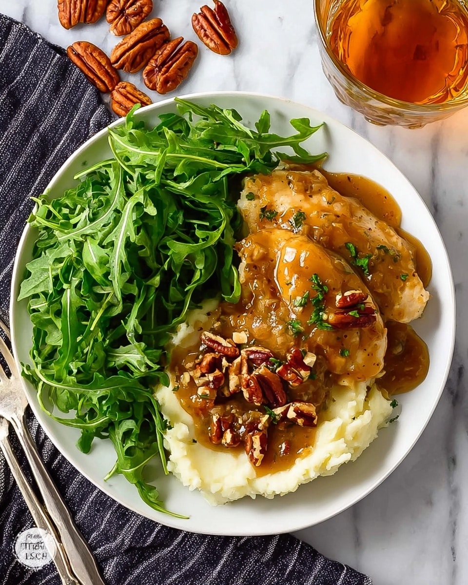 The image shows a white plate with three main parts: a large pile of green leafy arugula on the top half, smooth white mashed potatoes on the bottom left, and two browned chicken breasts covered with thick brown gravy and sprinkled with chopped pecans on the bottom right, sitting on the mashed potatoes. The plate is on a white marbled surface with a dark striped cloth underneath. There are some whole pecans scattered nearby and a glass with a light amber drink in the top right corner. Photo taken with an iphone --ar 4:5 --v 7