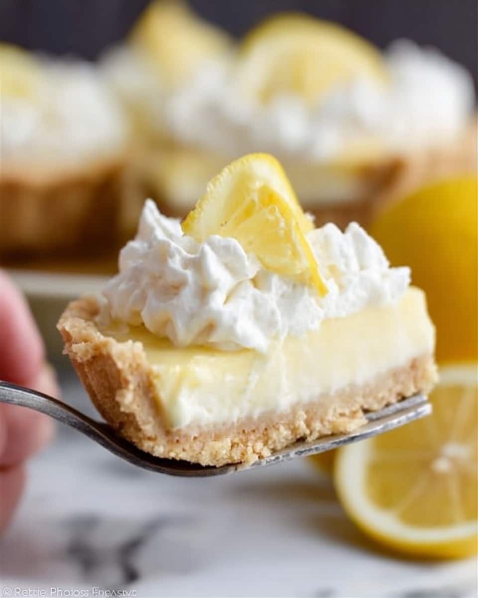 A close-up of a creamy lemon tart slice held by a woman's hand on a fork. The tart has three layers: a crumbly light brown crust at the bottom, a thick smooth pale yellow lemon filling in the middle, and a fluffy white whipped cream topping decorated with small dollops. On top of the whipped cream is a small wedge of lemon for garnish. More lemon tarts and cut lemon halves are blurred in the white marbled background. The photo has soft natural light and highlights the texture of the whipped cream and lemon filling. Photo taken with an iphone --ar 4:5 --v 7