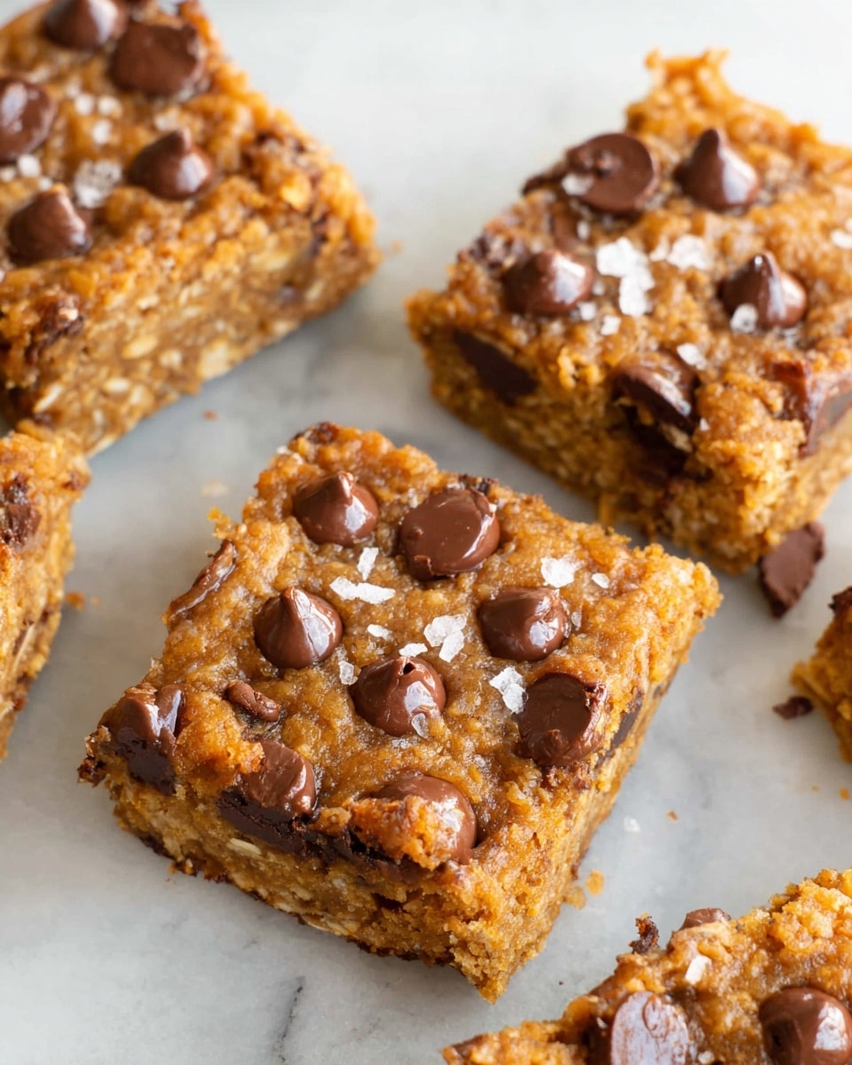 The image shows several square cookie bars with a golden brown, slightly crumbly top layer studded with glossy, melted chocolate chips that create a rich texture. The thick bars have a moist, dense middle layer speckled with oat-like grains, giving a chewy look. Some flakes of coarse white sea salt are scattered over the top, adding contrast and hinting at a salty-sweet flavor. The bars rest on a smooth, white marbled surface, arranged close together to show their uneven edges and soft interior. photo taken with an iphone --ar 4:5 --v 7