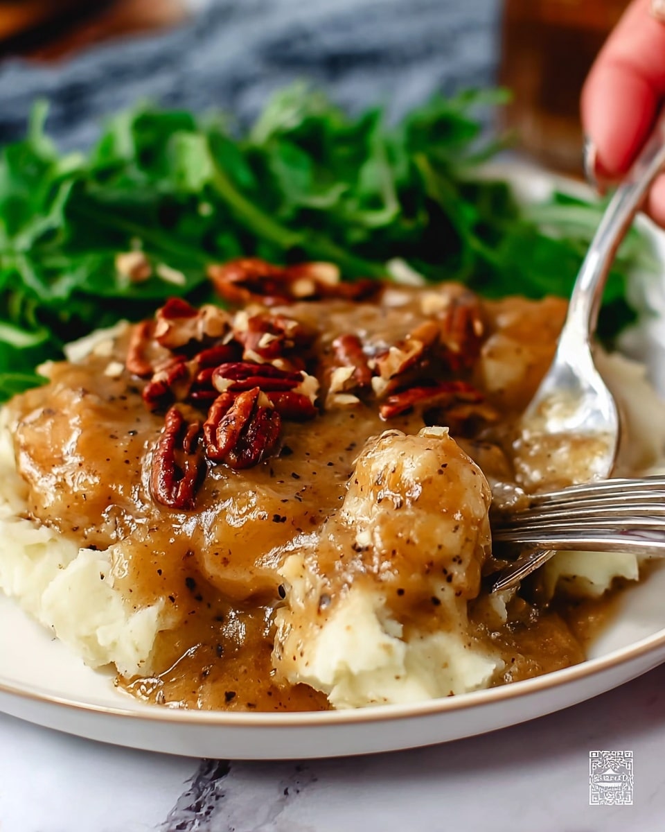 The dish is served on a white plate with a white marbled surface underneath. It has three main layers: the bottom layer is creamy, pale mashed potatoes with a smooth texture. On top of the potatoes is a thick layer of brown gravy with visible black pepper specks and small chunks, giving it a rich, slightly glossy look. The third layer consists of chopped pecans scattered on top of the gravy. In the background, there is a small pile of fresh green leafy vegetables adding a pop of color. A shiny silver fork with a woman's hand holding it is placed on the side, touching the mashed potatoes and gravy. photo taken with an iphone --ar 4:5 --v 7