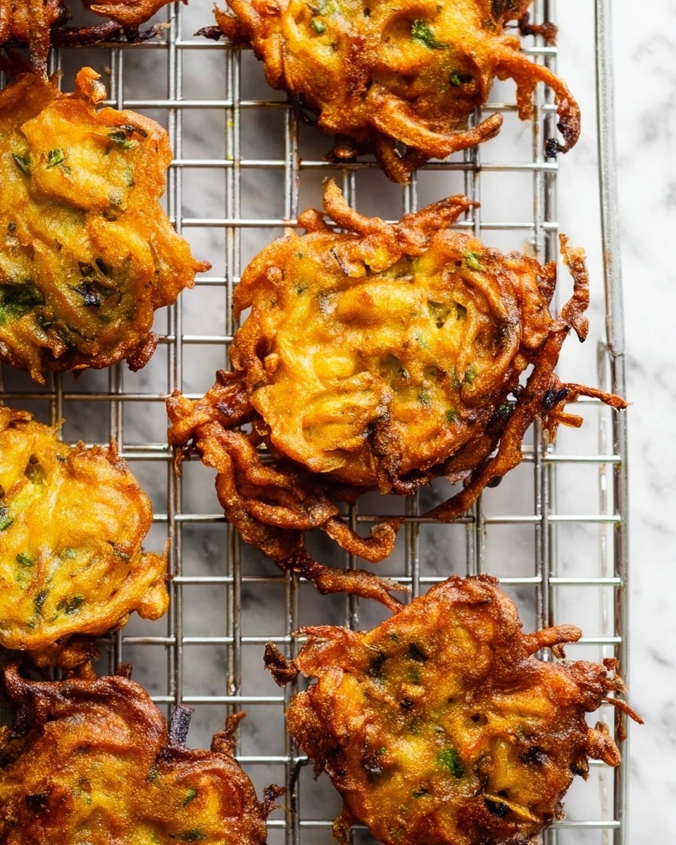 The image shows a metal cooling rack with several crispy, golden-brown fritters stacked on it. Each fritter has a rough texture with visible pieces of green herbs mixed into the batter. The fritters are irregularly shaped with curly edges and some parts appearing more browned than others, giving a crunchy look. The cooling rack is placed on a white marbled surface, and the fritters are spaced apart, allowing the texture and color variations to be clearly seen. photo taken with an iphone --ar 4:5 --v 7