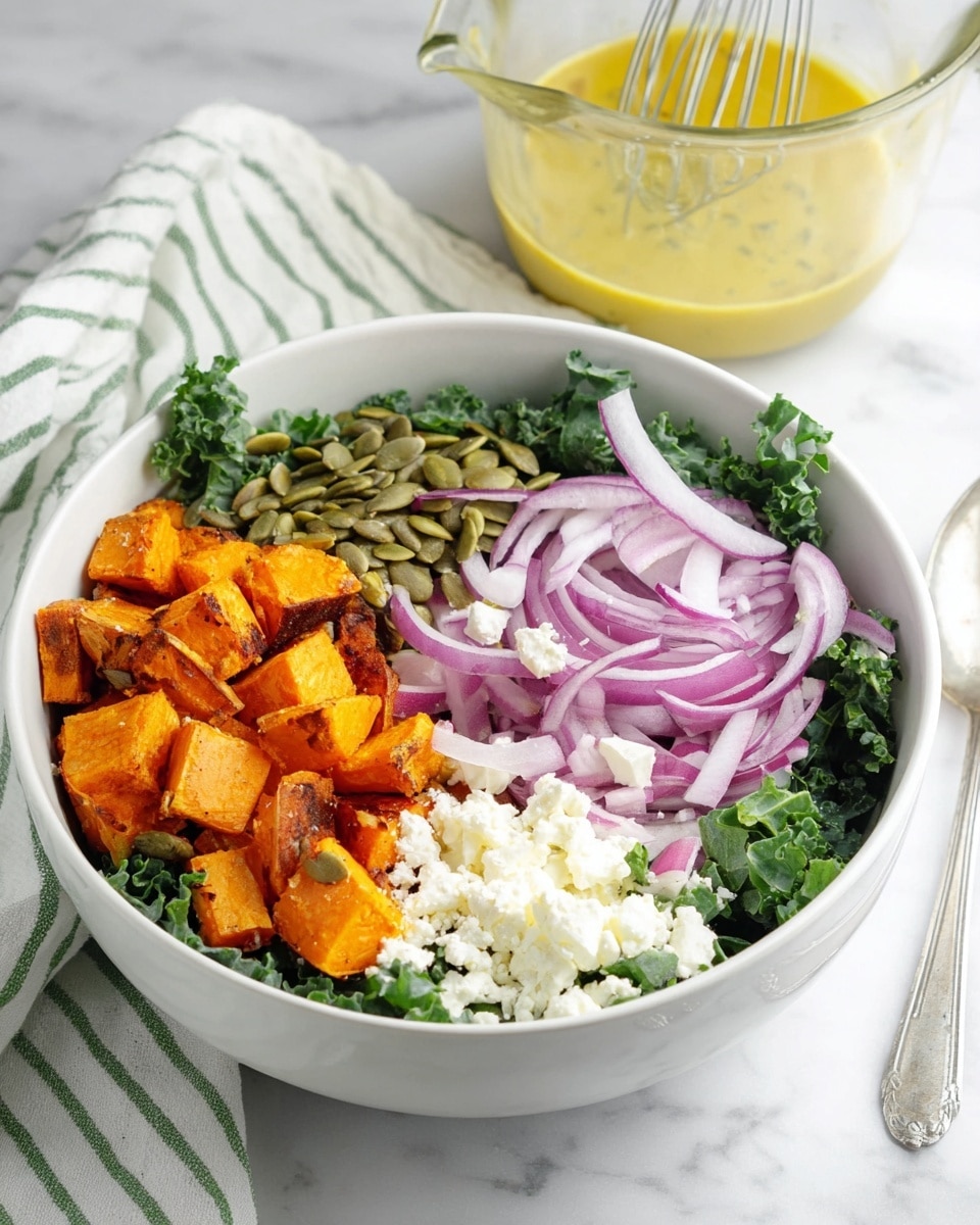 A white bowl holds a fresh salad with a base layer of dark green kale leaves. On top, there are four distinct sections: bright orange roasted sweet potato cubes with a slightly charred texture on the left, thinly sliced purple and white red onion rings next to them, a small pile of light green pumpkin seeds below the onions, and a heap of crumbly white cheese on the right. Behind the bowl, there is a glass measuring cup filled with a light yellow dressing and a whisk inside it, all set on a white marbled surface with a white cloth featuring green stripes in the background. photo taken with an iphone --ar 4:5 --v 7