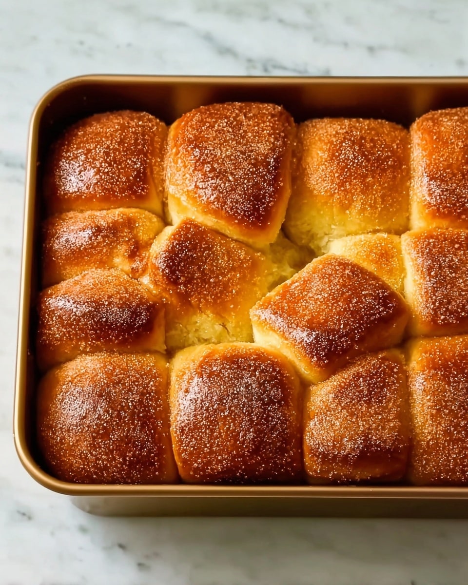 The image shows a golden-brown pull-apart bread inside a rectangular metal baking pan. The bread has multiple large, soft-looking pieces, separate but closely packed, with a shiny, slightly sugar-coated crust on top. The edges of each bread piece are darker golden, and the bread appears fluffy and moist inside. The pan rests on a white marbled surface. photo taken with an iphone --ar 4:5 --v 7