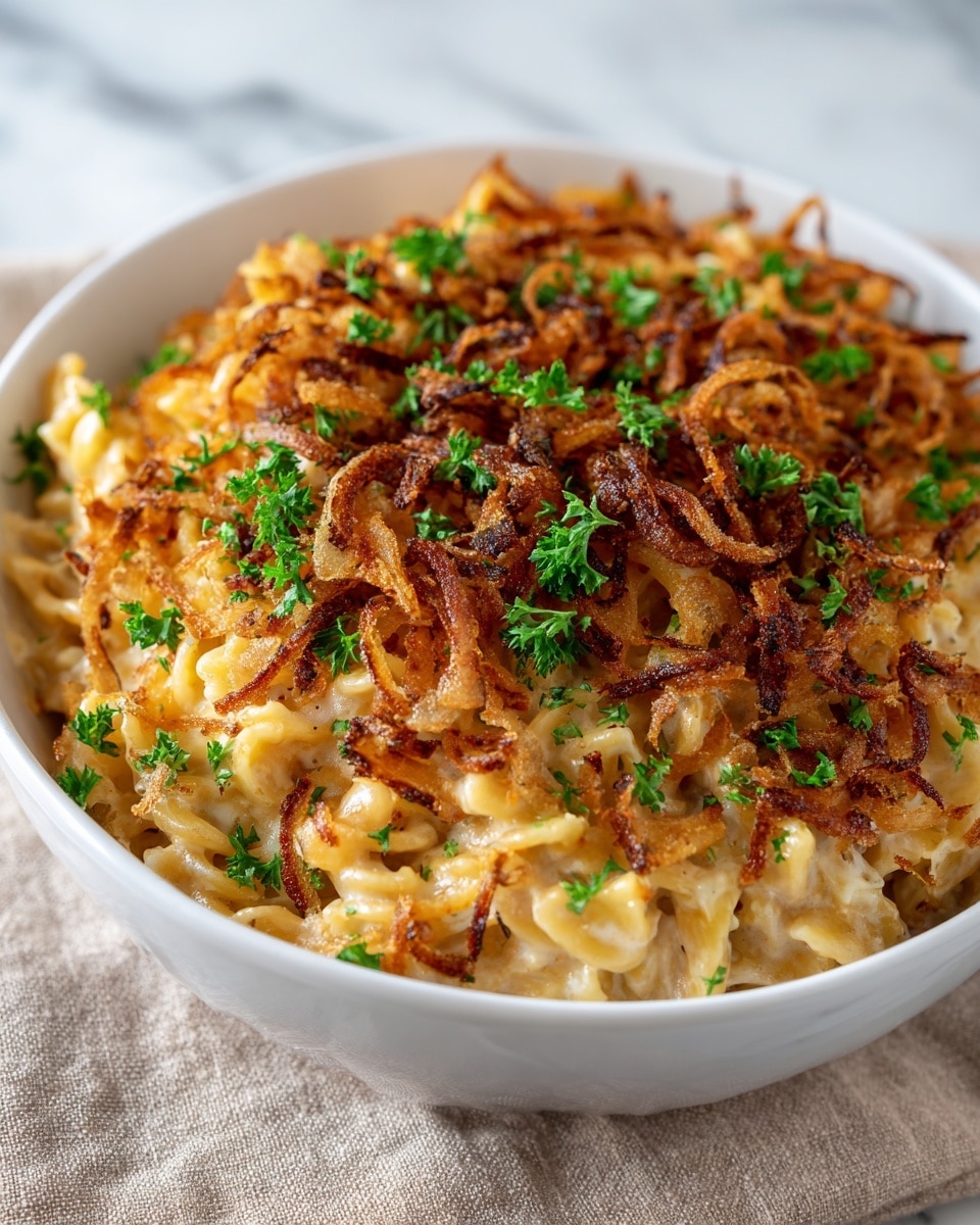 A white bowl filled with creamy pasta layers, starting with soft, golden brown pasta mixed with melted cheese that looks smooth and rich. On top, there is a layer of crispy fried onions, browned and crunchy with a mix of dark and light brown colors, scattered unevenly. Sprinkles of fresh green parsley leaves are spread over the top, adding a fresh color contrast. The bowl rests on a soft textured cloth, all placed on a white marbled surface. photo taken with an iphone --ar 4:5 --v 7