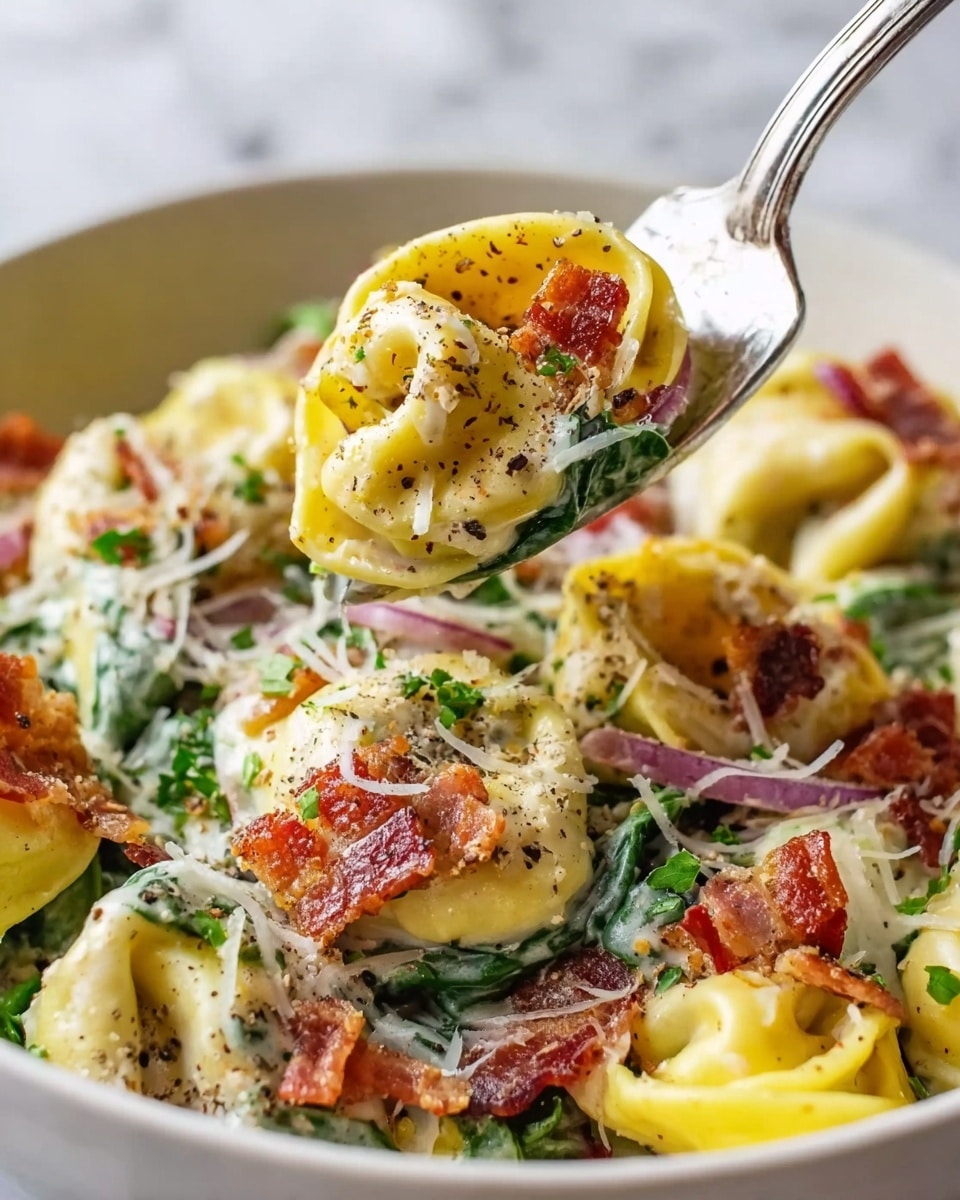 The image shows a close-up of creamy tortellini pasta layered over fresh green spinach and thin slices of purple onion. The tortellini layers are yellow with a smooth texture and are coated in a white creamy sauce. Crispy, brownish-red bacon pieces are scattered over the top, adding a crunchy contrast to the soft pasta. Freshly grated white cheese sprouts over the pasta, and a sprinkle of black pepper and green herbs adds color and texture on top. A shiny silver fork holds up a close view of a stuffed tortellini piece, further highlighting the sauce and crispy bacon. The bowl is white, set on a white marbled surface. photo taken with an iphone --ar 4:5 --v 7