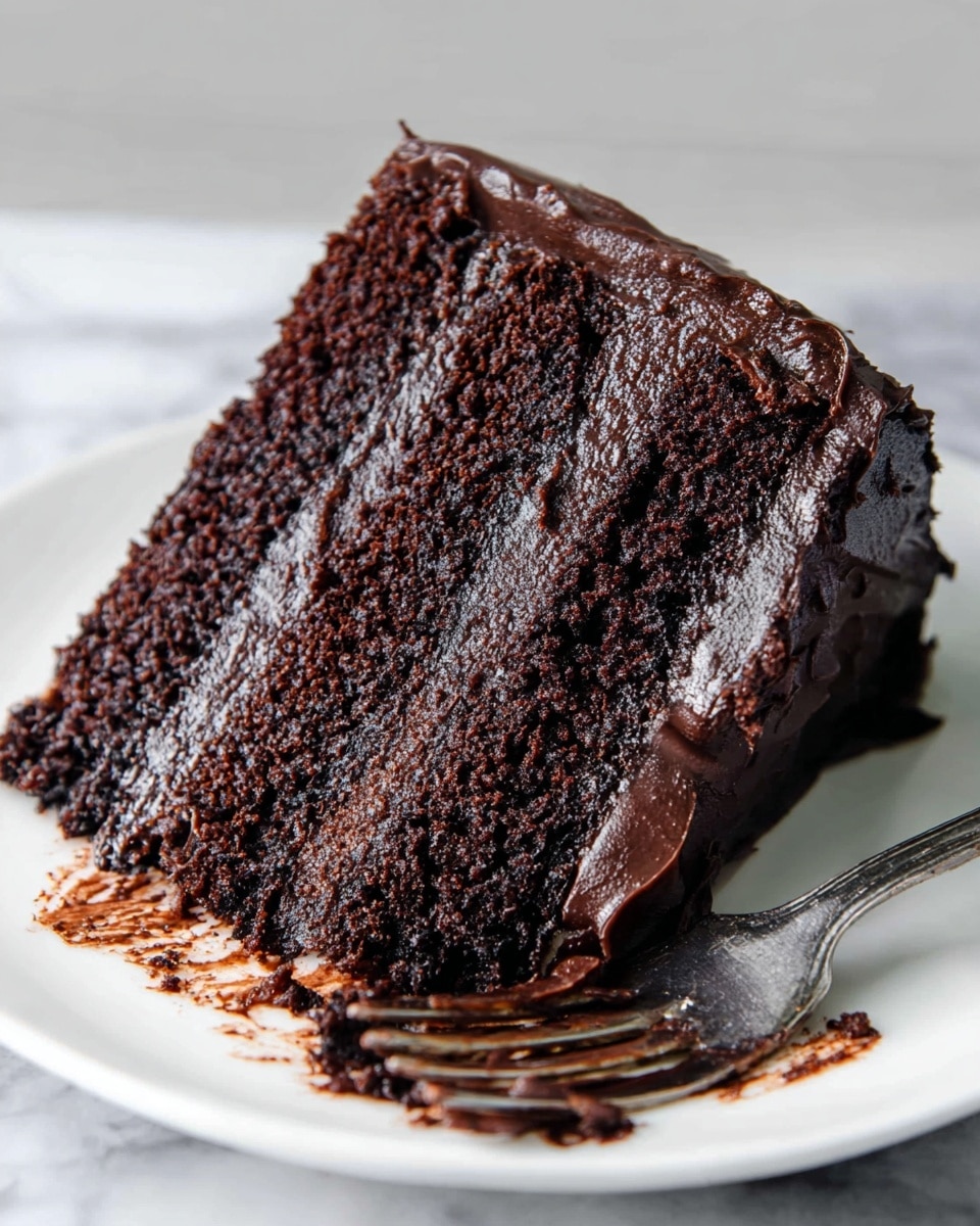 A close-up view of a single slice of rich chocolate cake with three thick, moist layers in dark brown color. Each layer is filled and covered with smooth, glossy dark chocolate frosting that looks slightly shiny and thick. The cake slice sits on a white plate with some crumbs around it, and a silver fork with chocolate smears lays next to the slice. The backdrop is a white marbled texture. photo taken with an iphone --ar 4:5 --v 7