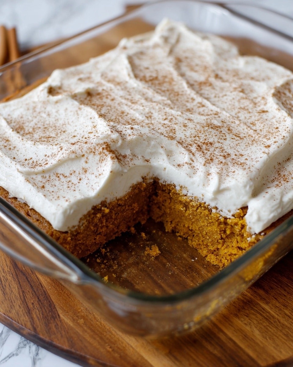 This image shows a rectangular glass baking dish with a pumpkin cake inside, where one piece has been cut and removed from the front left corner. The cake has one main thick layer, which is a moist, dense, orange-brown pumpkin cake base. On top is a thick layer of smooth, white cream cheese frosting spread evenly and topped with a light dusting of brown cinnamon powder. The dish is set on a wooden board with a white marbled textured background visible in parts. Photo taken with an iphone --ar 4:5 --v 7