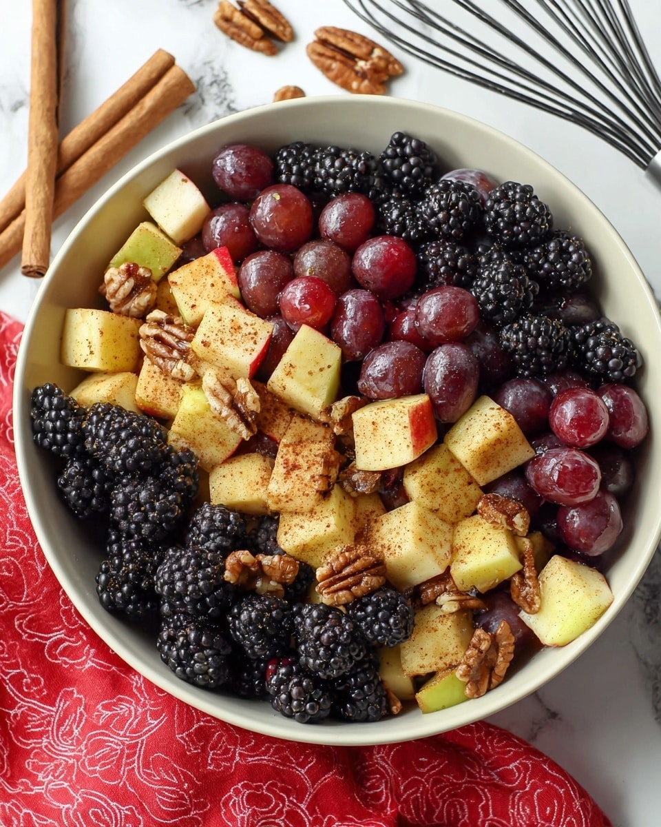 A close-up view of a white bowl filled with a fruit and nut mix, featuring three main layers: large, light yellow apple chunks coated with cinnamon powder scattered throughout, dark purple-black blackberries clustered between the apples, and shiny red grapes interspersed evenly. Small pieces of brown pecans are sprinkled on top, adding texture and contrast. The bowl sits on a white marbled surface with two cinnamon sticks placed beside it. The colors are warm and natural, showing the fresh, juicy, and slightly spiced appearance of the ingredients. Photo taken with an iphone --ar 4:5 --v 7