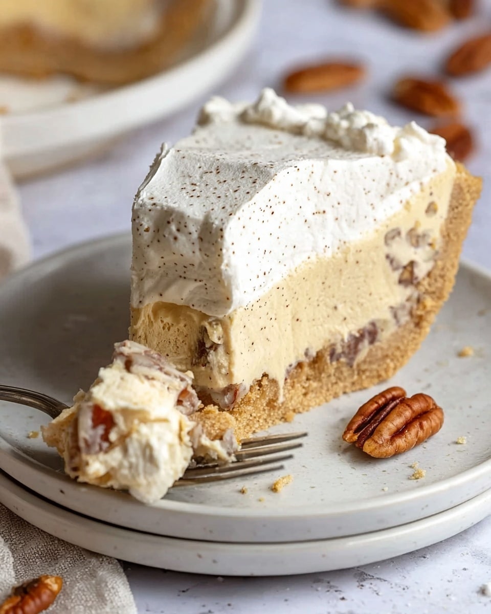 A slice of pie on a white plate shows three layers: a crumbly light brown crust around the edge, a creamy pale yellow filling with visible pecan pieces mixed inside in the middle, and a thick white whipped topping with tiny dark specks on top. A silver fork rests on the plate, holding a small piece of the pie with layers of cream and whipped topping. The plate sits on a white marbled surface with some scattered pecans blurred in the background. The photo taken with an iphone --ar 4:5 --v 7