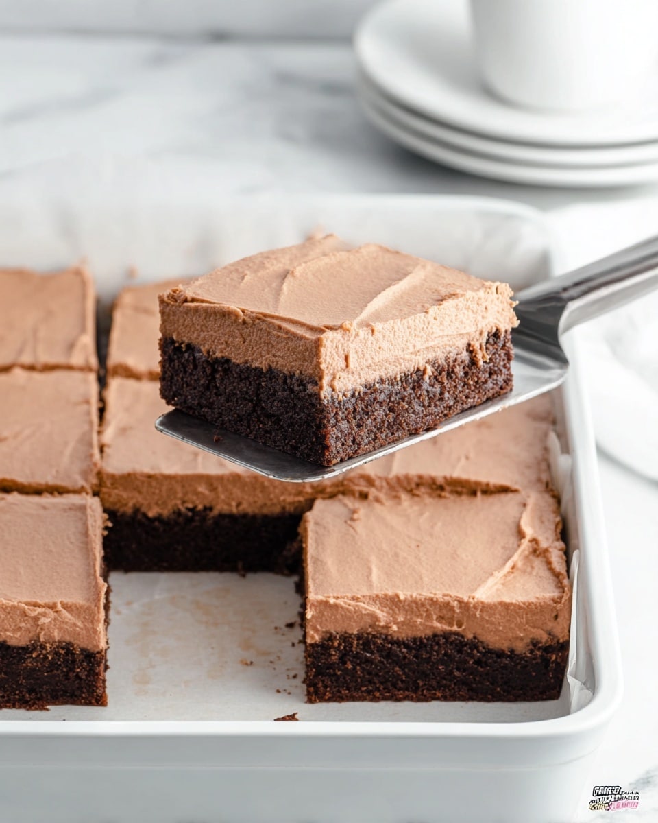 A square piece of chocolate dessert with two clear layers sits on a silver spatula; the bottom layer is a dark, dense brownie, while the top layer is a thick, smooth light brown frosting spread evenly across the surface. This piece is being lifted from a white baking pan that holds the rest of the dessert, which is cut into square pieces with visible clean edges. The background and surface show a white marbled texture, and in the top corner, a few stacked white plates and a white cup are slightly visible. Photo taken with an iphone --ar 4:5 --v 7
