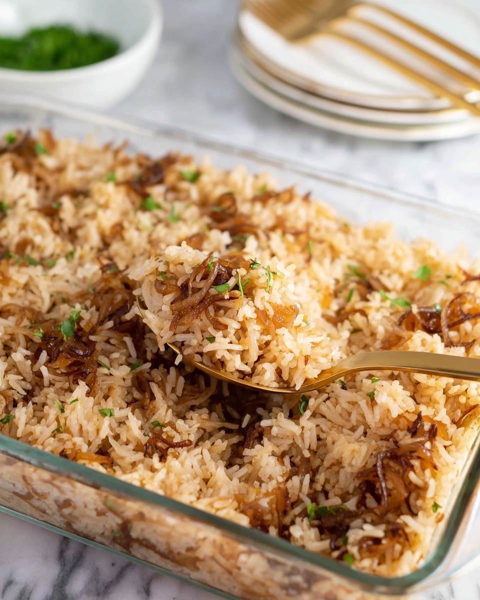 A close-up view of a white bowl filled with cooked rice mixed with small chunks of caramelized onion and scattered green herb leaves, likely parsley, adding a touch of color. The rice grains are light brown, with a slightly glossy texture, showing a mix of soft and slightly firm grains. In the middle, a golden spoon is partially buried in the rice, ready to serve. The bowl is placed on a white marbled surface with part of a black and white patterned cloth visible underneath. photo taken with an iphone --ar 4:5 --v 7