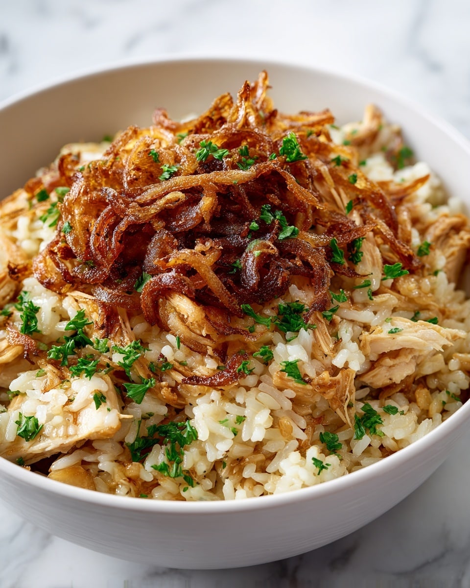 A close-up view of a creamy rice dish served in a white bowl, showing a thick layer of cooked rice mixed with tender pieces of light golden chicken. On top, there is a generous layer of crispy, caramelized onions with a rich brown color and slightly curled texture, sprinkled with small bright green parsley pieces adding fresh color contrast. The rice underneath is soft and glossy, with a light golden tint from the sauce coating every grain evenly. The bowl is set against a white marbled surface, highlighting the dish’s warm and inviting colors. photo taken with an iphone --ar 4:5 --v 7