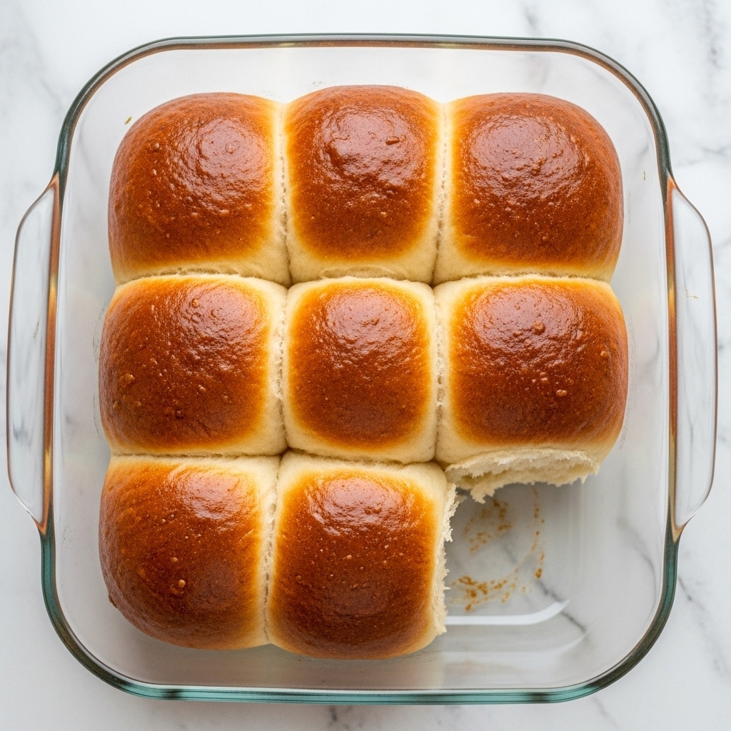 A close-up of several golden brown soft bread rolls with a shiny, smooth top layer, showing a fluffy and light inside texture where one roll is pulled apart, revealing the airy, soft layers within. The rolls are placed in a light beige cloth inside a light-colored woven basket on a white marbled surface, with natural light highlighting the warm tones and textures of the bread. Photo taken with an iphone --ar 4:5 --v 7