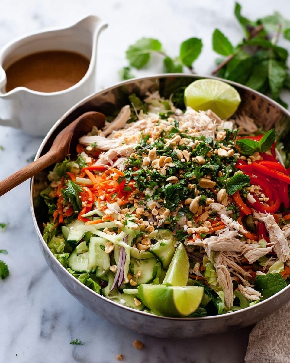 The image shows two white bowls filled with a fresh, colorful salad placed on a white marbled surface. Each bowl contains several layers starting with a base of green leafy lettuce, followed by sliced cucumbers, shredded chicken pieces, thin strips of orange carrot, and thinly sliced red onions. The salad is topped with crushed peanuts and small chopped red chili pieces. A lime wedge is placed on the edge of the top bowl, along with sprigs of fresh leafy herbs. Beside the bowls, there is a small white sauce jug filled with brown dressing, and a pair of red chopsticks rests on the edge of the top bowl. Photo taken with an iphone --ar 4:5 --v 7