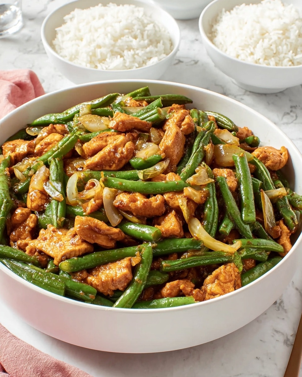 A large white bowl filled with a stir-fry dish showing two main layers: the first layer consists of chopped green beans with a smooth and shiny texture, and the second layer consists of orange-brown cooked chicken pieces scattered evenly among the beans, both coated lightly in a glossy sauce; small pieces of translucent cooked onion are interspersed within the dish. In the background, there are two white bowls filled with plain white rice placed on a white marbled surface next to the main bowl. photo taken with an iphone --ar 4:5 --v 7