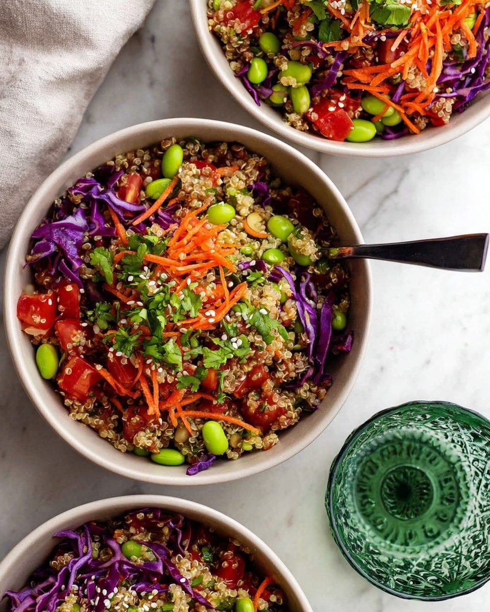 Three white bowls filled with a colorful quinoa salad are placed on a white marbled texture. Each bowl contains layers including light beige quinoa, bright green edamame beans, shredded orange carrots, chopped red tomatoes, and bits of purple cabbage. Fresh green herbs and sprinkled white sesame seeds are added on top. A black spoon is in the top right bowl. Near the bowls is a clear green glass with intricate patterns. The setting is bright and fresh. photo taken with an iphone --ar 4:5 --v 7
