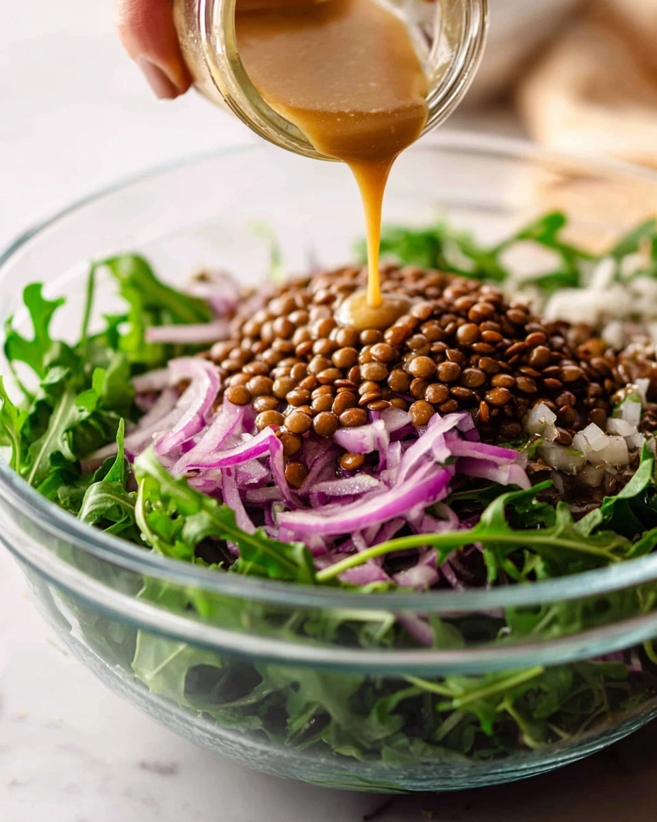 A white plate holds a salad with three main layers: the base is fresh green leafy vegetables, topped with a layer of brown lentils mixed in with thinly sliced light purple onions, and scattered on top are roasted orange sweet potato chunks with slightly darkened edges. A silver spoon with a detailed handle rests on the salad, slightly sticking out. In the background, a white bowl with dark brown candied nuts sits on a white marbled surface, along with a glass jar of light brown dressing and a small white bowl of creamy white sauce. A gray cloth napkin is draped casually under the plate and near the bowl. Photo taken with an iphone --ar 4:5 --v 7