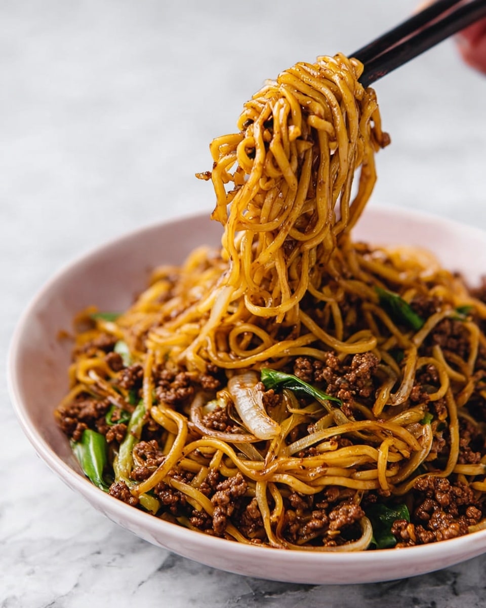 A close-up of a white bowl filled with a generous serving of stir-fried noodles mixed with ground beef, translucent cooked onion slices, and small pieces of green vegetables. The noodles are golden brown, coated with a glossy sauce, and lifted in the air by a pair of black chopsticks held by a woman's hand. The background features a white marbled surface that contrasts with the rich colors of the dish. photo taken with an iphone --ar 4:5 --v 7